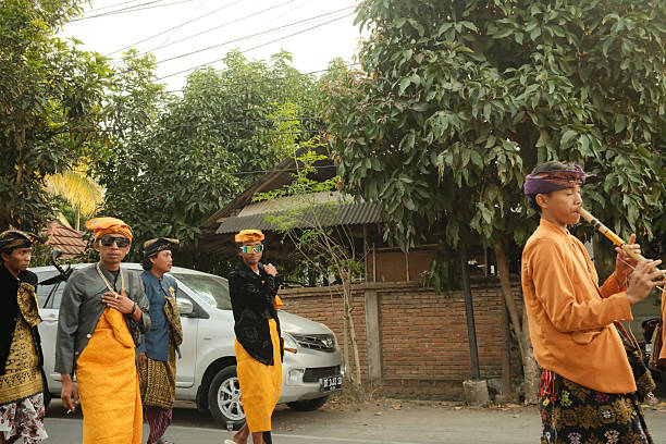 Lombok Island, Indonesia - September 07, 2025: Balinese men in traditional clothing walking in a ceremony procession, one playing a flute, on a street in Indonesia