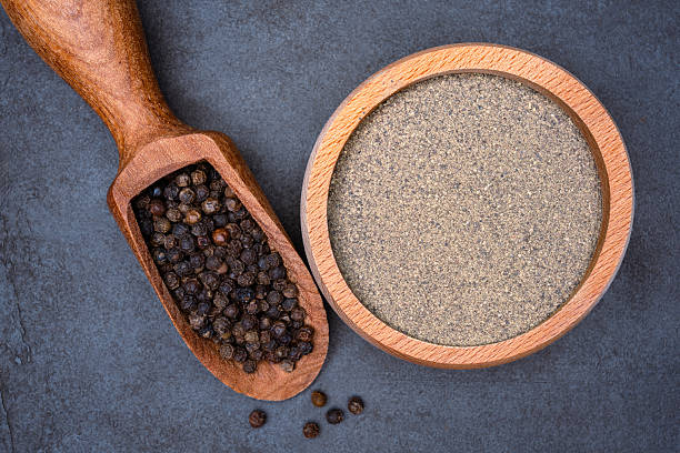 istock Black peppercorns  and ground black pepper powder on black background 2239942247
