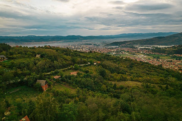 Scenic aerial view of a valley town nestled by green hills under a cloudy sky