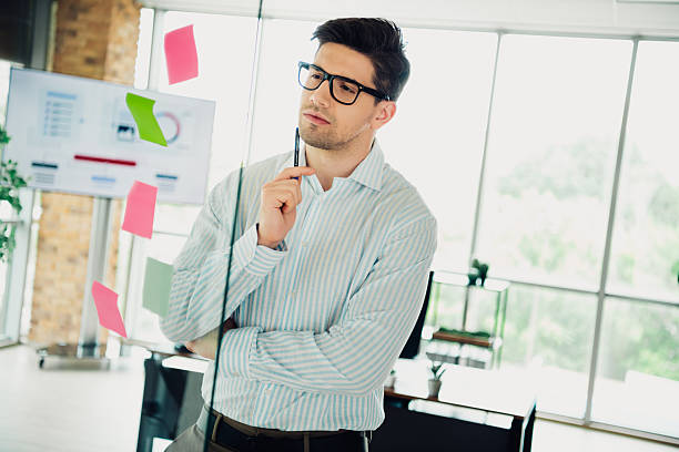 istock Young professional businessman brainstorming ideas in office workspace environment with glass wall and sticky notes 2239944237