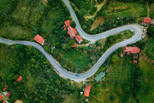 Aerial view of a car traveling on a serpentine road surrounded by houses and trees
