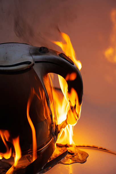 A electric kettle engulfed in flames, with the fire brightly illuminating its surface and rising upward. a dangerous situation, with dense tongues of fire covering its body.