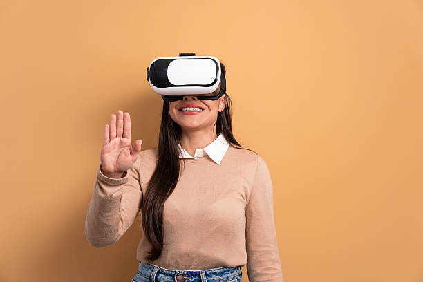 istock cheerful brunette young woman Using VR headset and gesturing in beige colors. virtual reality, technology simulation concept. 2239951518