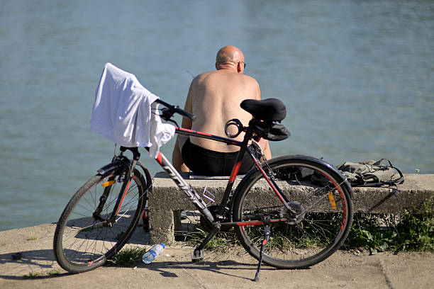 A man sitting on a bench by the water with a bicycle nearby in Belgrade, Serbia on 6 June 2024