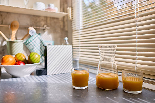 Refreshing orange juice in glasses and a carafe on a kitchen counter, illuminated by natural morning sunlight creating striped patterns through window blinds