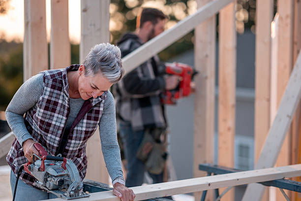 istock Older Woman Using Circular Saw on Wood Frame at Construction Site with Builder in Background 2239956691