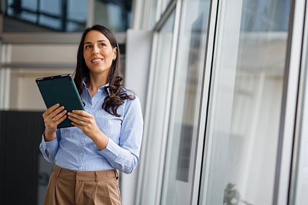 istock Businesswoman holding tablet, looking up with thoughtful expression in modern office environment 2239958418