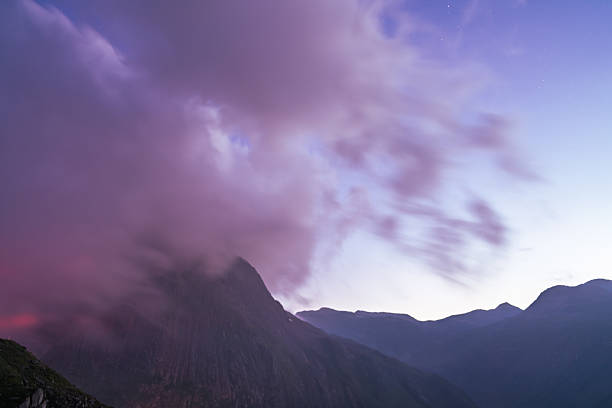 Peaceful twilight over the Swiss Alps, captured from Furka Pass. The mountain silhouettes fade into soft pastel hues of purple and orange, while the first stars appear in the evening sky above the rugged alpine peaks.