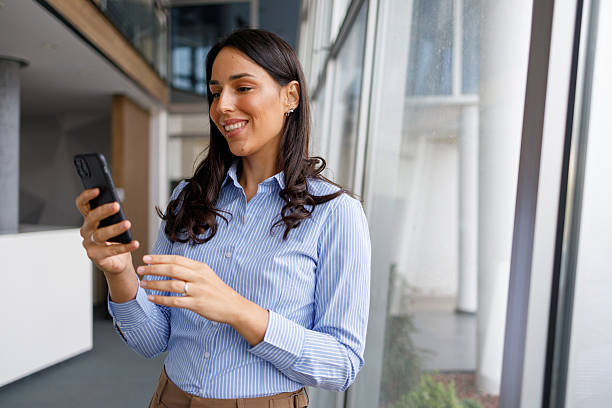 istock Professional businesswoman smiling while sending message on smartphone, communicating online in modern office 2239959039