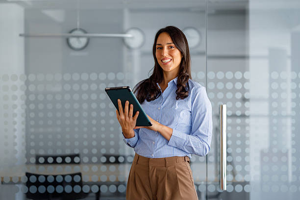 istock Smiling business woman holding a digital tablet while standing in a modern office, enjoying her corporate work 2239961666