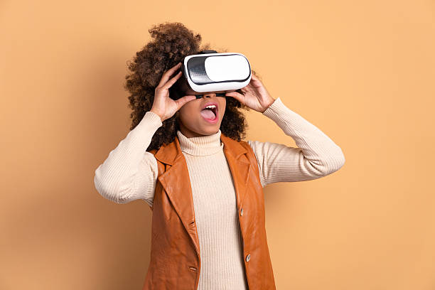 istock surprised afro brazilian woman Using VR headset and gesturing in beige colors. virtual reality, technology simulation concept. 2239962904
