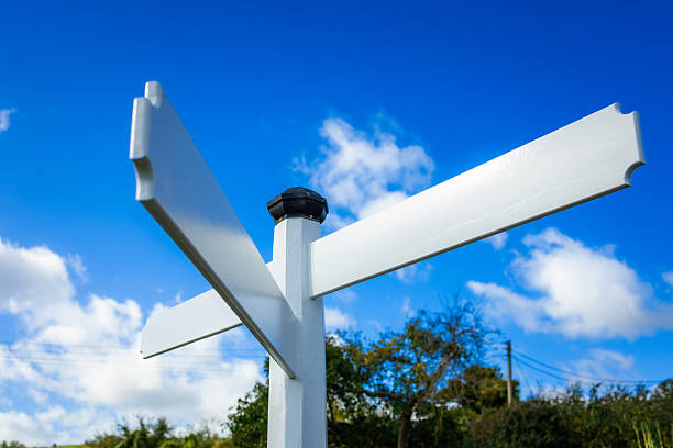 A blank white directional sign stands at a crossroads in the English countryside.