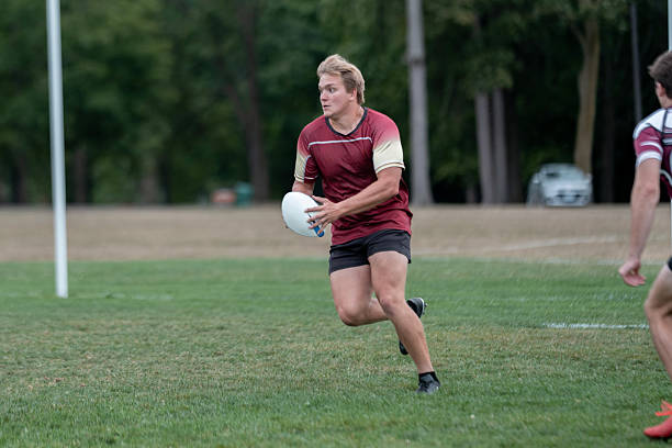 istock Athletic Rugby Player In Maroon Jersey Runs With Ball On Grass Field 2239964259