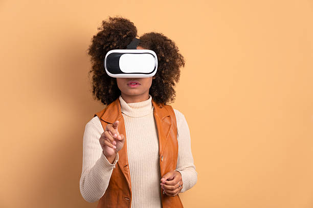 istock excited black young woman Using VR headset and gesturing in beige background. virtual reality, technology simulation concept. 2239965030