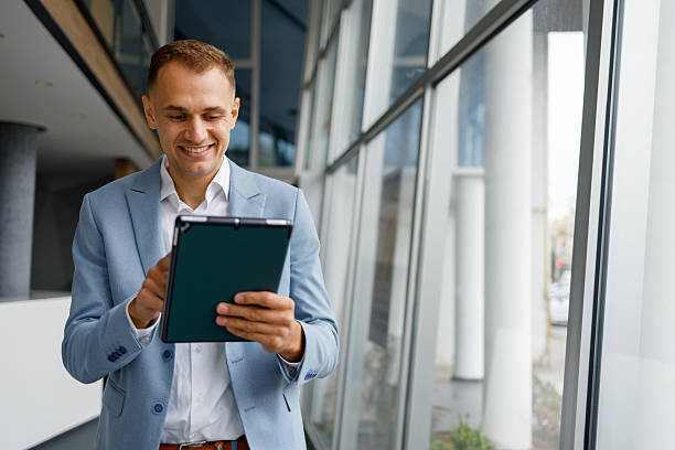 istock Businessman smiling, standing in modern office building and using a digital tablet for work 2239969161