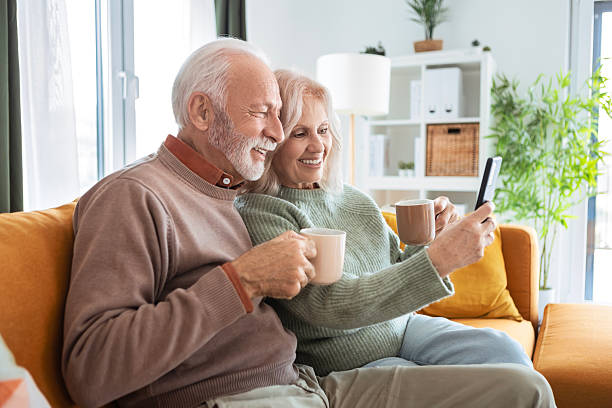 istock Smiling Elderly Pair Enjoying Time Indoors Using Phone 2239969633