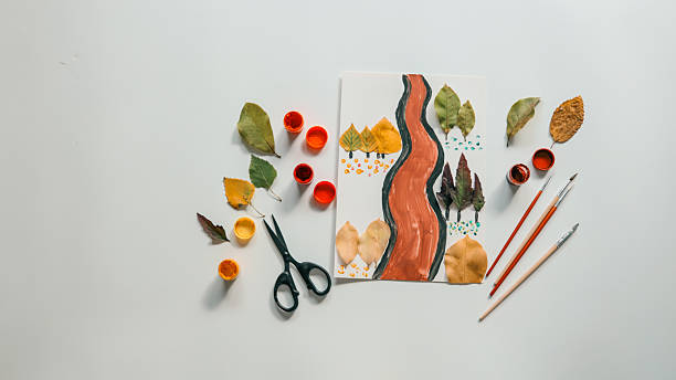 Autumn-themed artwork with leaves, paint, and brushes on a white surface.