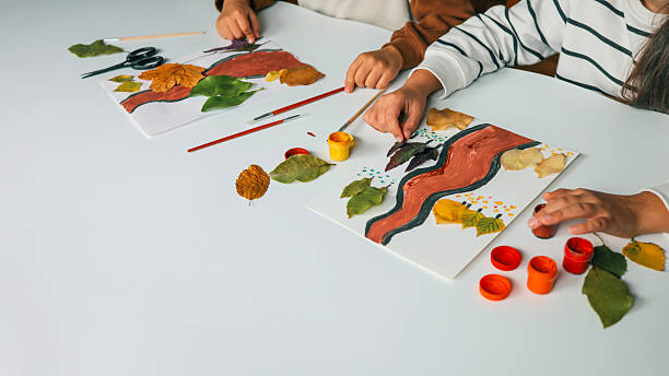 istock Children creating art with leaves and paint on a white table. 2239971565