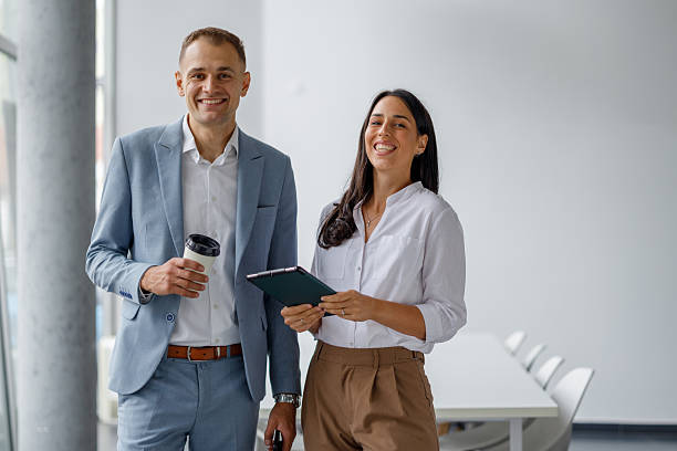istock Business colleagues smiling in a modern office, carrying coffee and a tablet, ready for a meeting 2239972508