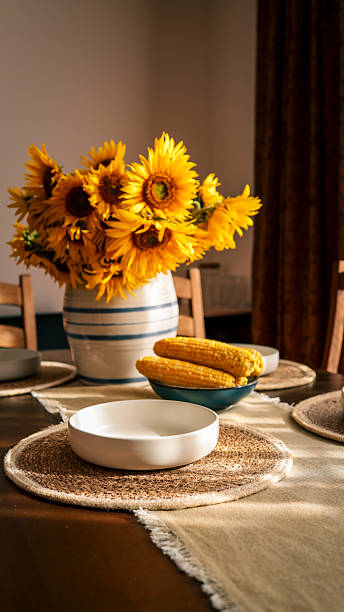 A beautiful dining table setting with sunflowers and corn on the cob.