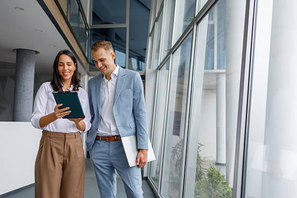 istock Business colleagues collaborating on digital tablet, discussing project while walking in modern office hallway 2239973728