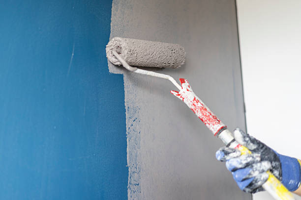 istock Hand painting wall with a roller, applying gray paint over blue color 2239975881