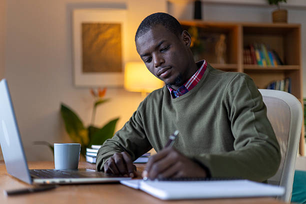 istock Focused young man writing at desk with laptop, studying or working from home 2239976402