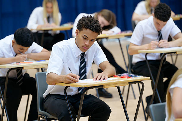 istock High school boy sitting at desk during exam writing in booklet, concentrating 2239976406