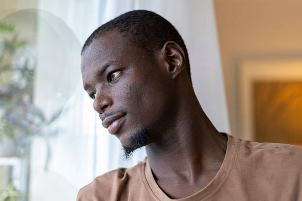 istock Young black man looking out a window, thinking and reflecting on his thoughts 2239977203
