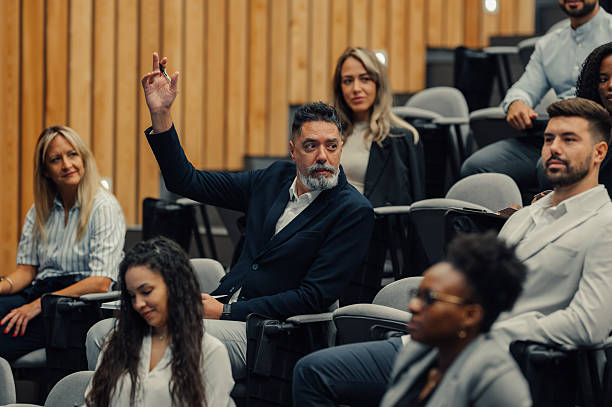 istock Mature man raising hand asking question at business conference 2239979955