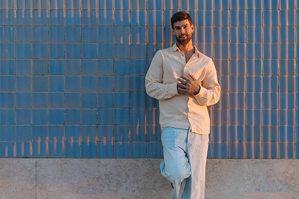 istock Young stylish man posing while leaning against a blue tiled wall during sunset 2239985375