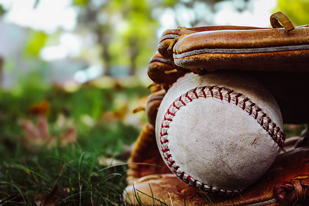 Baseball mitt filled with baseball balls sitting on the ball field in front of empty dugout during a sunset