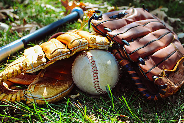 istock A baseball, bat, and two leather gloves are resting on a grassy field 2239990059