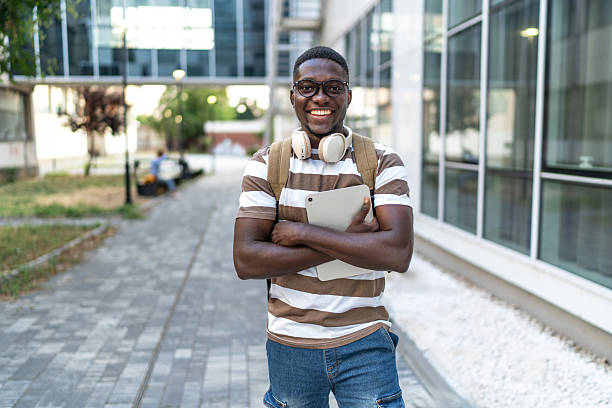 istock Young black man smiling at campus holding digital tablet 2239998340