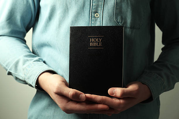 istock Man with hardcover Holy Bible on light background, closeup 2240003210