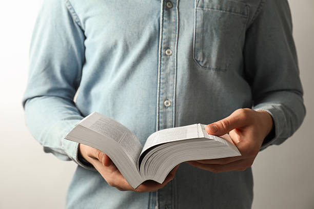 istock Man reading Holy Bible in English language on light background, closeup 2240003246