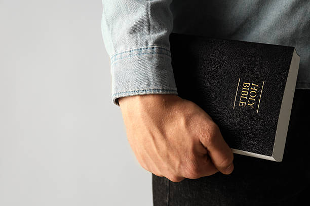 istock Man with hardcover Holy Bible on light background, closeup. Space for text 2240003247