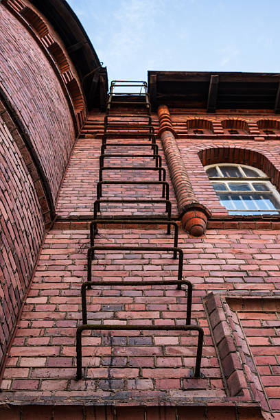 Rusty metal ladder on red brick industrial building.