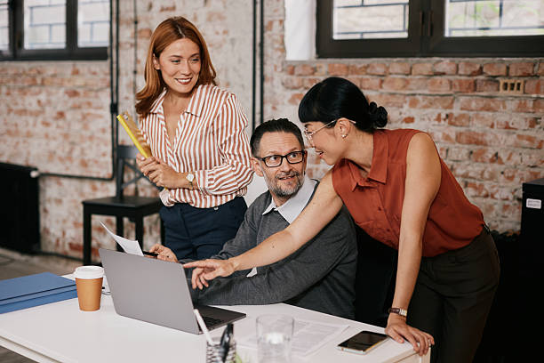 istock Mature professionals collaborating in modern office with laptop, coffee and documents, focused, in supportive mood 2240007002
