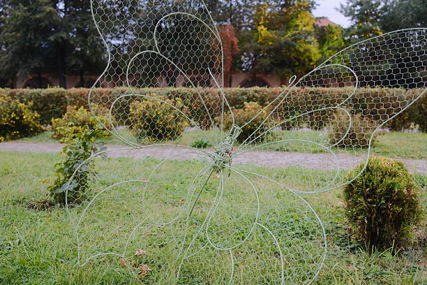 A wire mesh butterfly sculpture sits on a lawn near bushes.