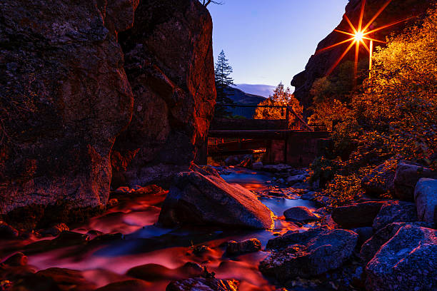 Night dusk view with street light reflecting in creek with soft silky water flowing downstream through large boulders.