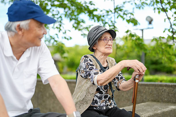 istock Two elderly people sitting on a bench, one wearing a hat 2240011862