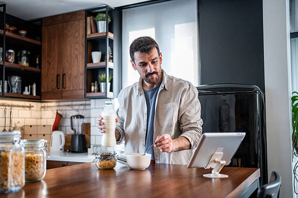 istock Man preparing breakfast cereal mixing milk and looking at tablet 2240012555
