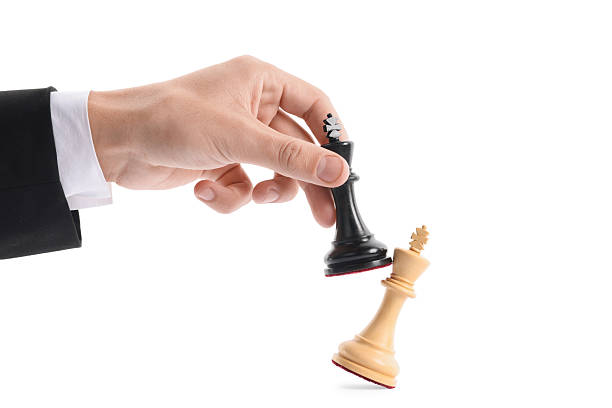 Man with black chess king knocking over white one on white background, closeup. Competition concept
