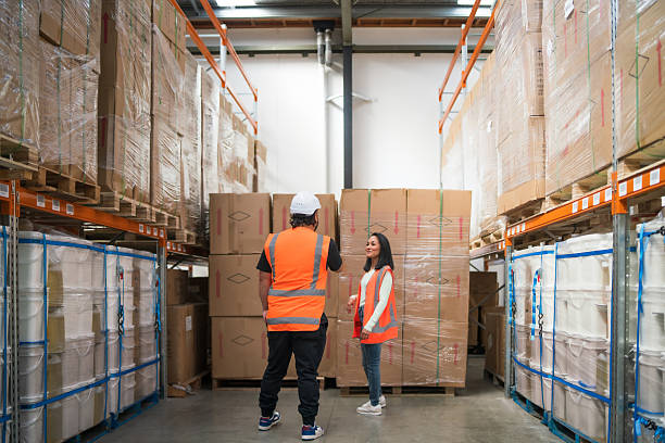 Logistics employees in reflective vests walk through a storage facility, collaborating to check and manage shipments efficiently.