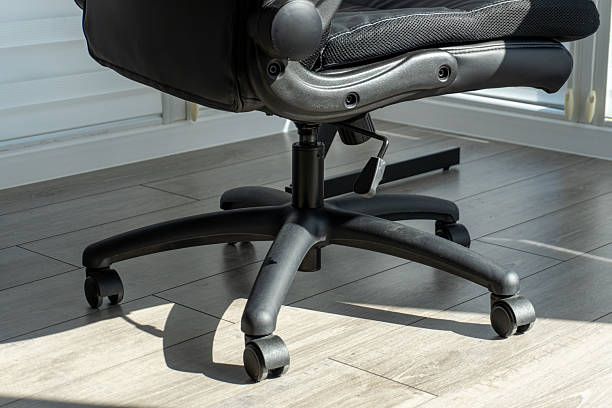 Modern black ergonomic office chair base with five wheeled casters on a light wooden floor under bright sunlight