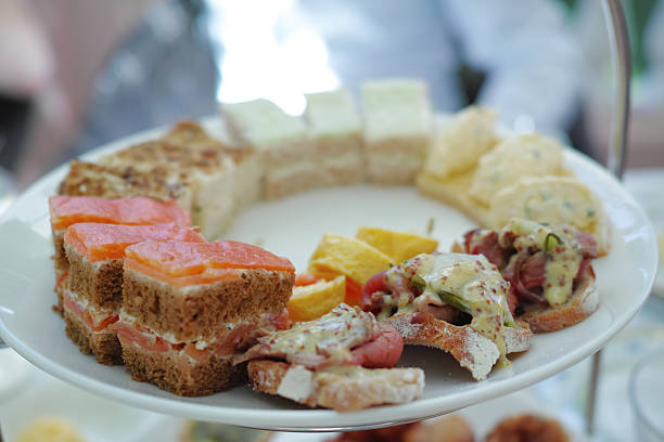 A delicious selection of finger foods served on a white plate, including sandwiches, gourmet toppings, and neatly arranged accompaniments. Ideal for depicting tea time gatherings or gourmet food styling.