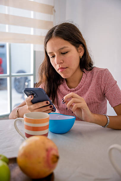 Young woman having breakfast while using phone and social media