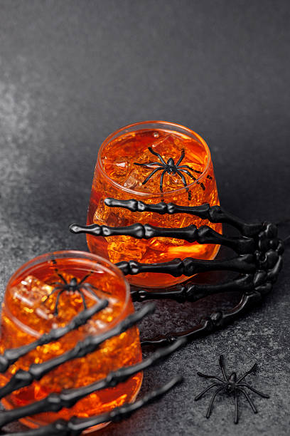 istock Two orange drinks with ice and spiders, skeleton hands around them, dark background 2240021158