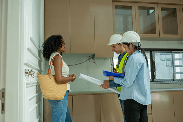 istock Female homeowner visits her new house under construction to inspect progress with an engineer and co-engineer reviews large blueprints, explaining details design and structure notes on a clipboard meet quality standards. 2240034999
